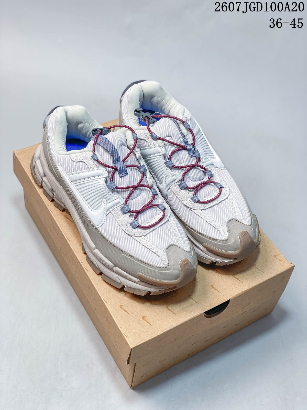 Pair of Nike Zoom Vomero Roam sneakers in white and grey with burgundy and blue laces, shown on a shoe box; image text shows style code 2607TGD100A20 and size range 36–45.