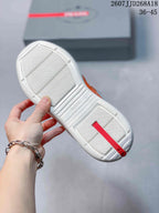 White outsole of an orange and gray sneaker showing textured tread, raised branding, and a red heel strip.