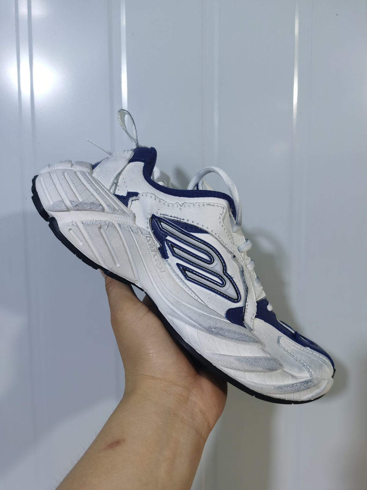 Angled view of the navy and white sneaker showing the layered upper, lace area, side emblem, and segmented outsole.