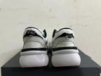 Rear view of white and light gray sneakers with black heel accents and a chunky white sole