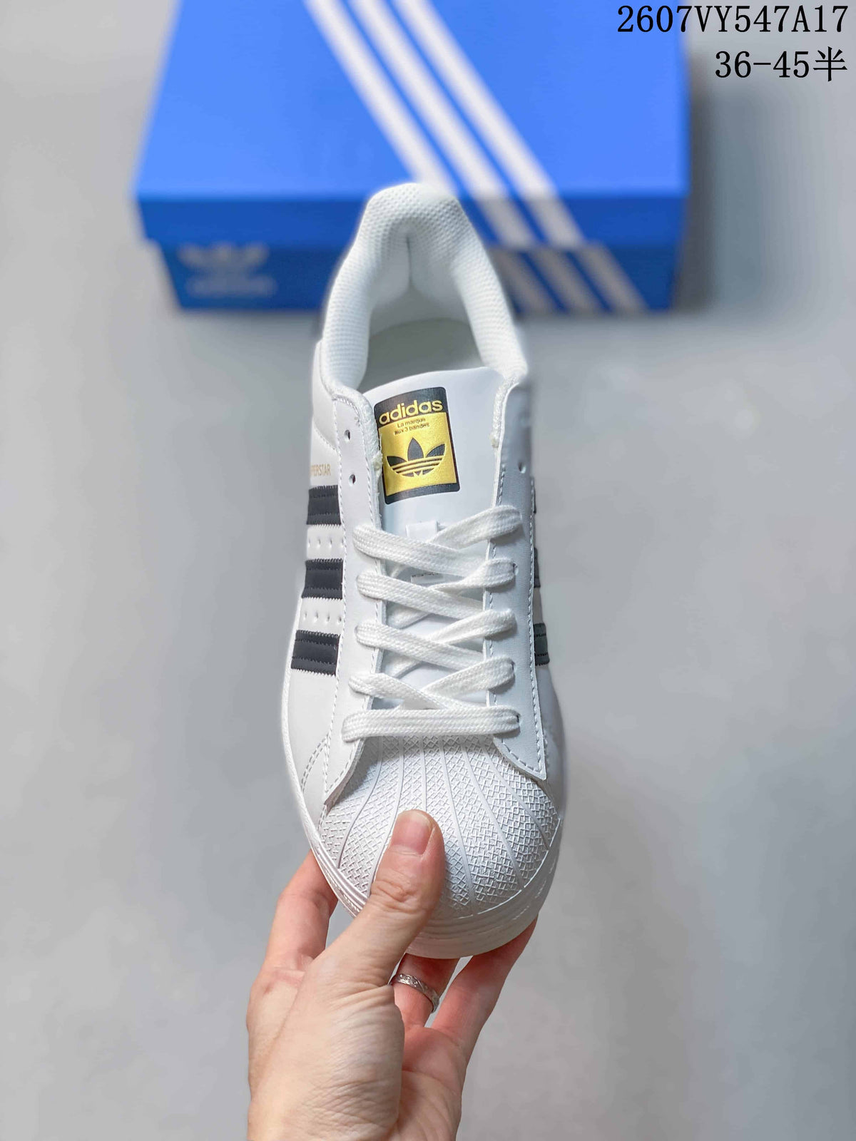 Front view of a white sneaker showing white laces, a textured shell-style toe, and a branded tongue label.