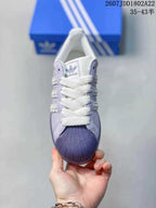 Top view of a lavender and white Adidas Superstar sneaker with white laces and textured toe cap.