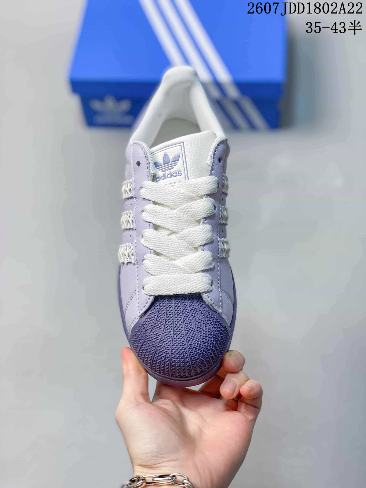 Top view of a lavender and white Adidas Superstar sneaker with white laces and textured toe cap.