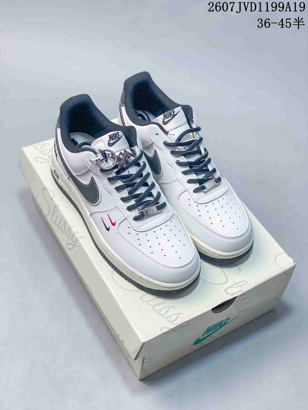 Pair of white Nike low-top sneakers with dark Swoosh details, patterned panels, dark laces, and decorative metal lace hardware displayed on a branded box.