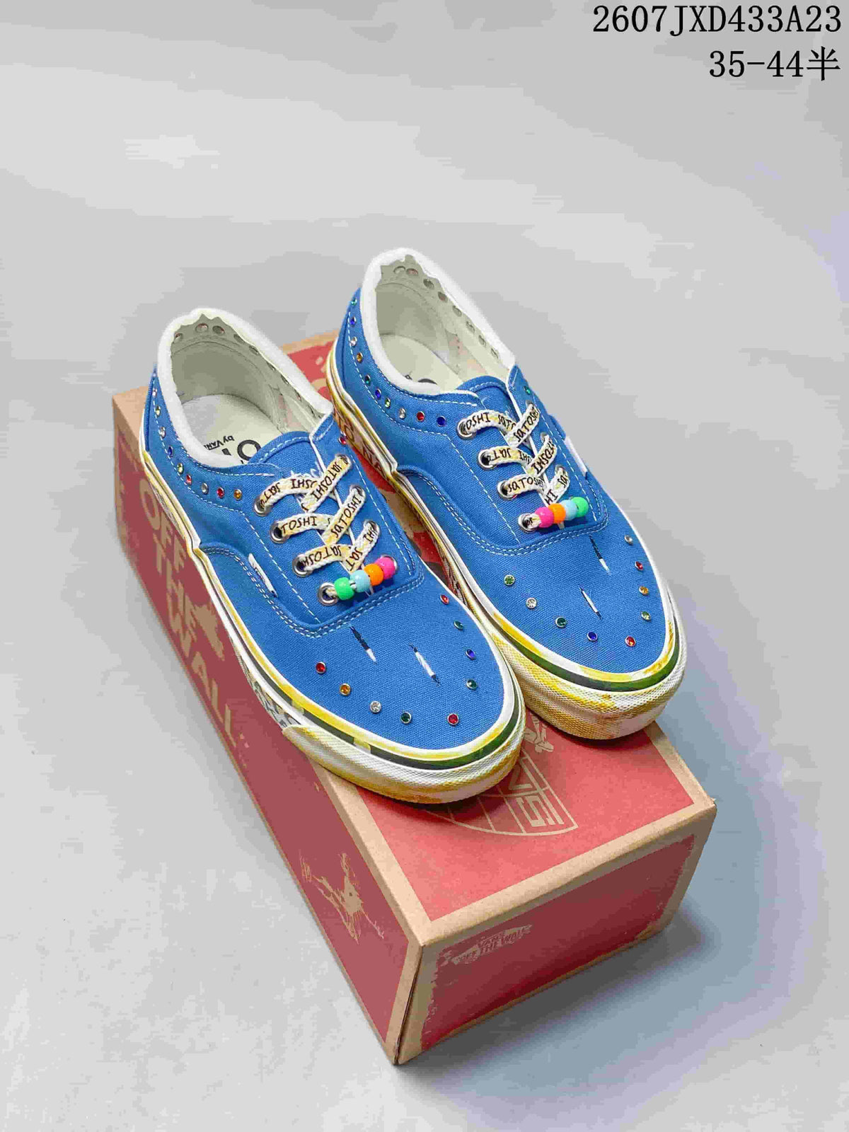Pair of blue Vans OG Era LX sneakers displayed on a shoebox, showing multicolor eyelets, beaded lace accents, and the printed style code and size range.
