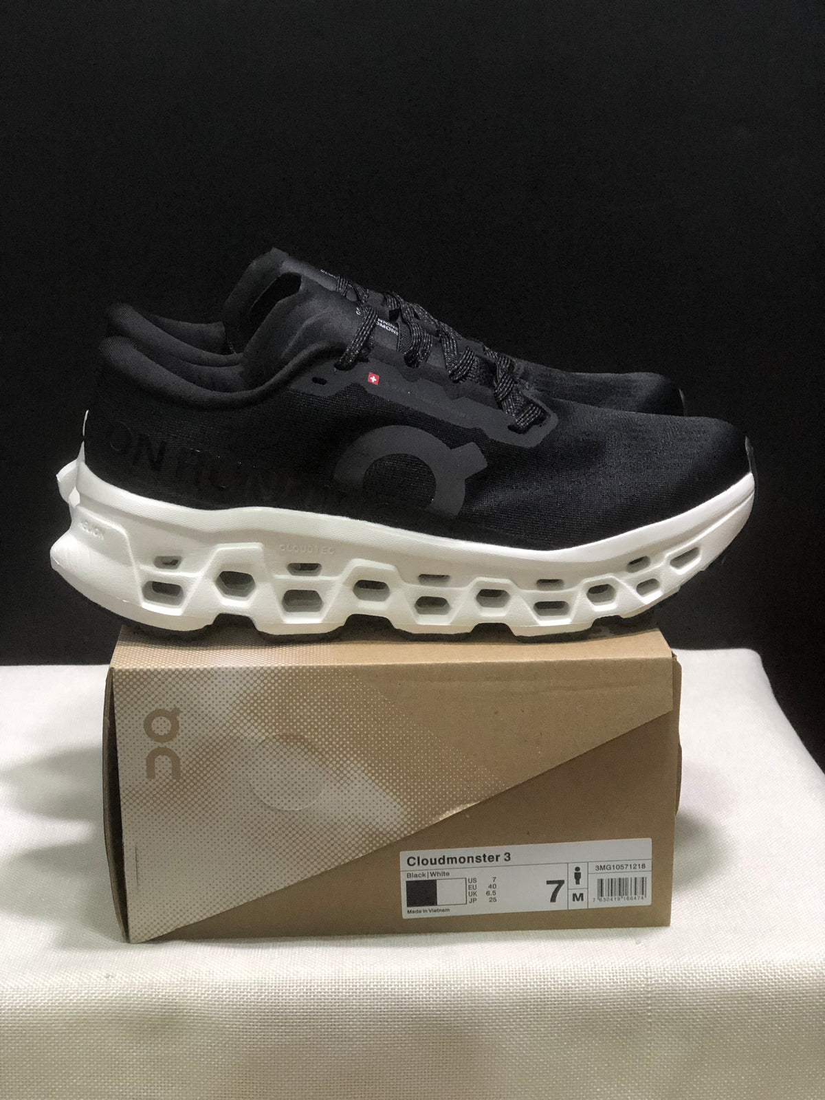 Side view of a black On Cloudmonster 3 sneaker showing the white open-structure midsole and shoe box label.