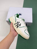 White and green low-top sneaker with a contrasting MLB-style side emblem, shown in hand in front of a branded box.