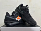 Pair of all-black Nike sneakers showing side profile, dotted Swoosh, and textured outsole