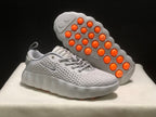 White sneaker shown with its underside facing upward, revealing orange circular outsole elements.