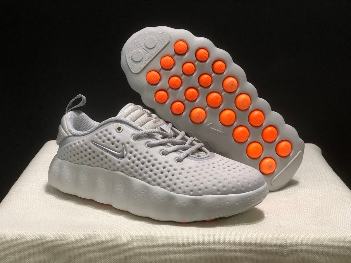 White sneaker shown with its underside facing upward, revealing orange circular outsole elements.