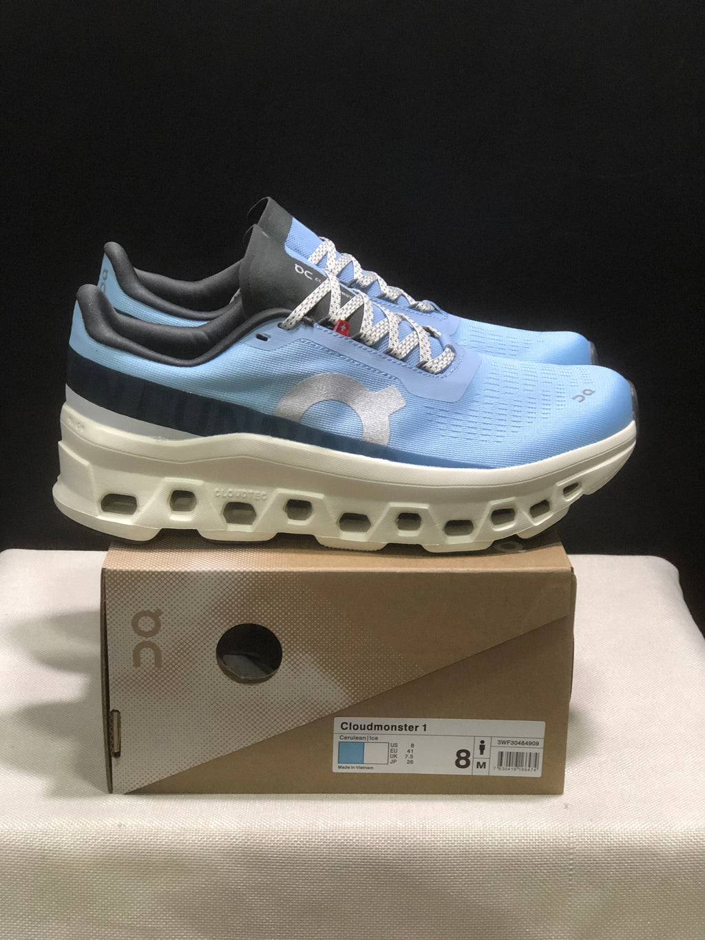 Side view of the light blue On Cloudmonster 1 sneakers with the thick white sculpted sole and product box.