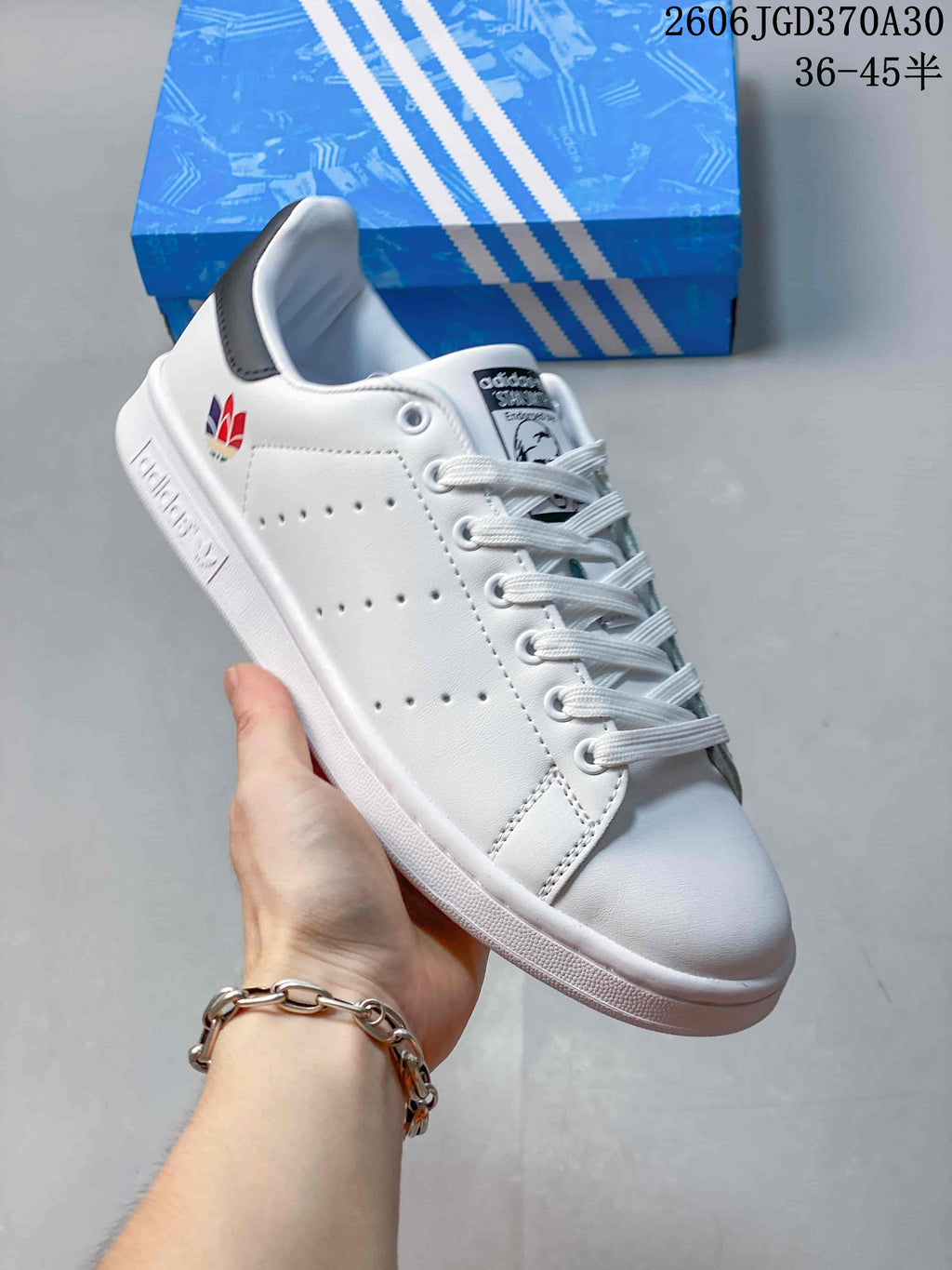 White Stan Smith-style sneaker with a multicolor heel emblem and a dark heel tab.