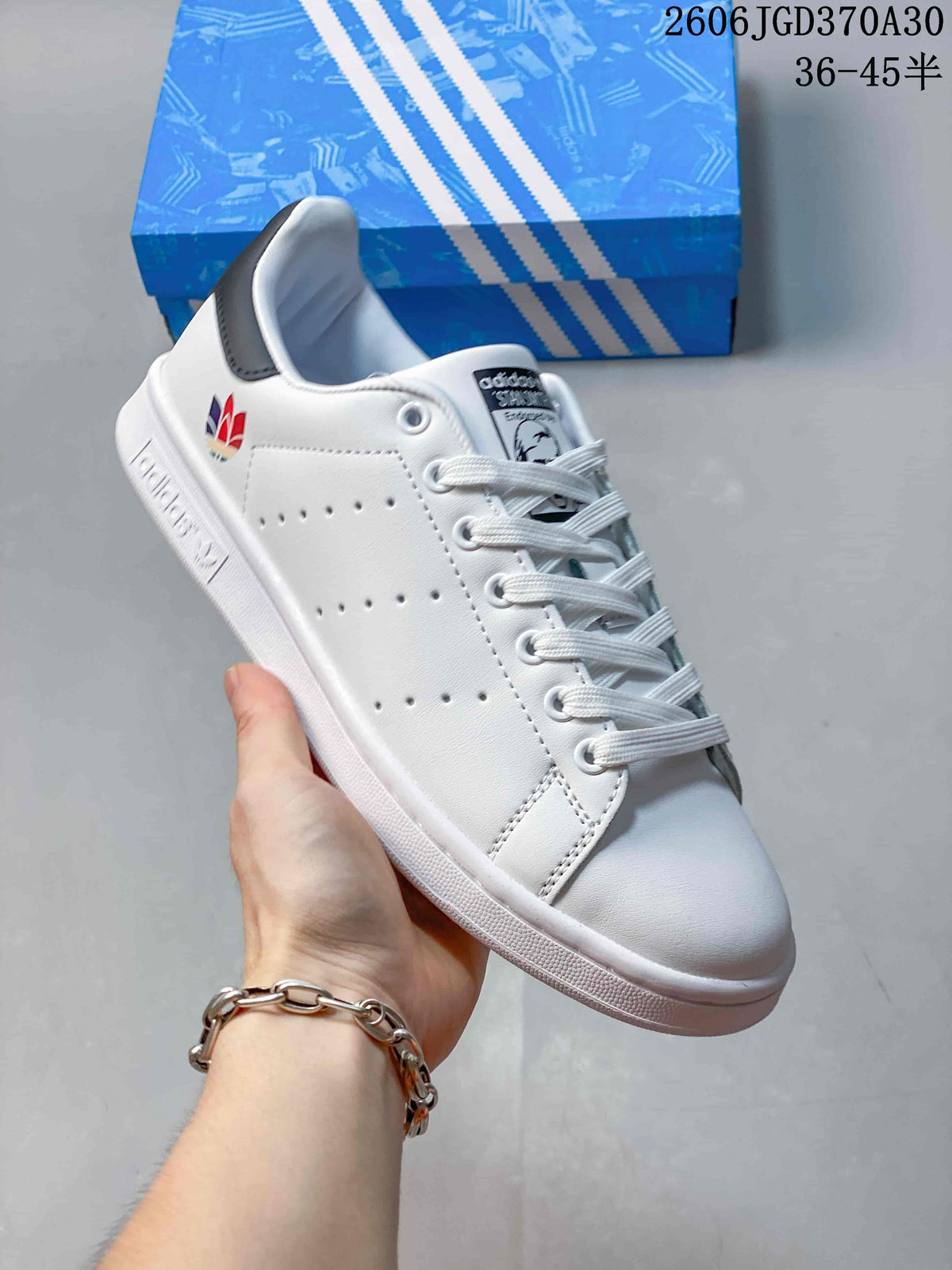 White Stan Smith-style sneaker with a multicolor heel emblem and a dark heel tab.