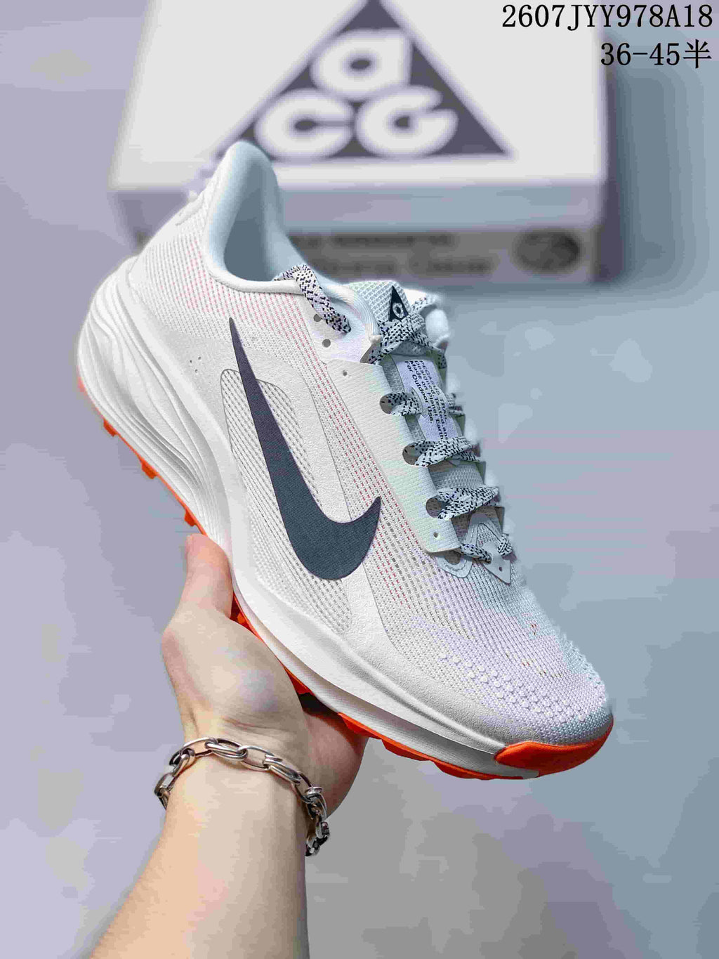 Angled side view of a Nike ACG Pegasus Trail shoe showing the dark Swoosh, light upper, patterned laces, and orange outsole edge.