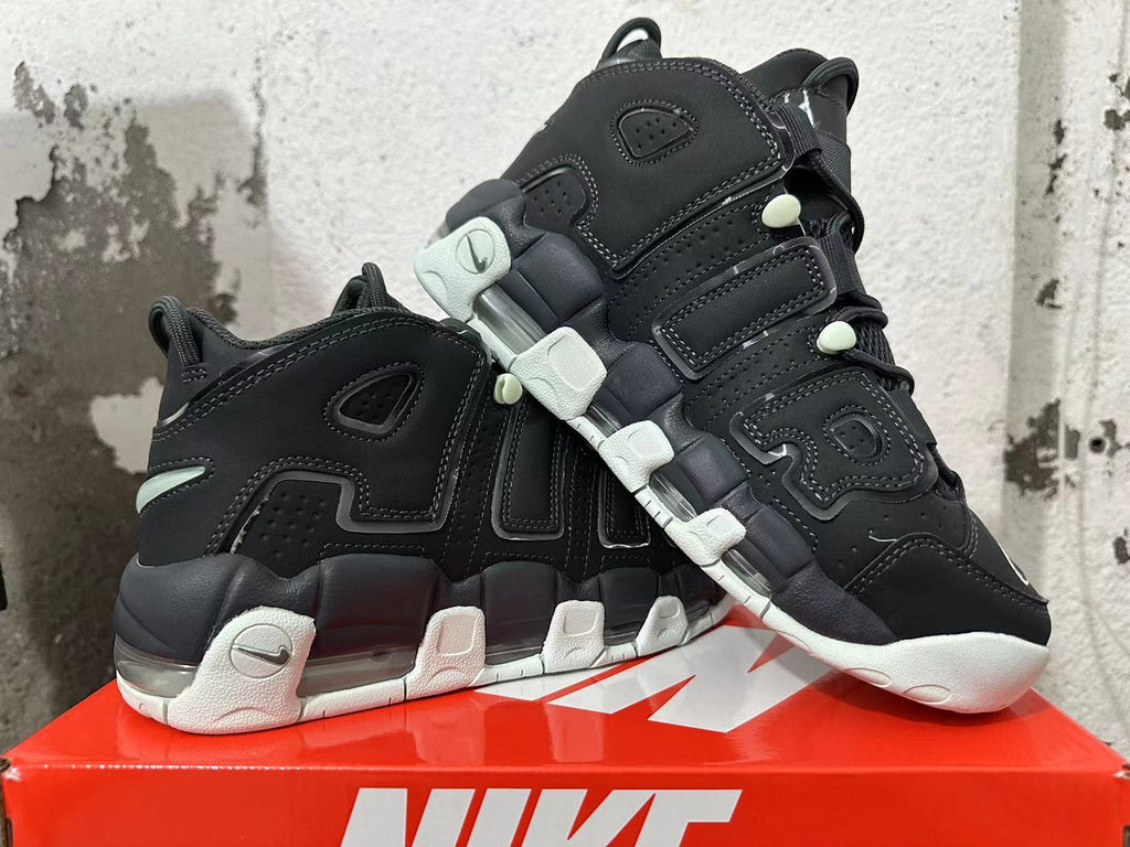 Pair of black Nike sneakers displayed from the side, highlighting oversized lettering, white outsole sections, and visible cushioning.