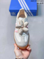 Top view showing the white and pink sneaker, suede-look toe panels, laces, and flower decoration.