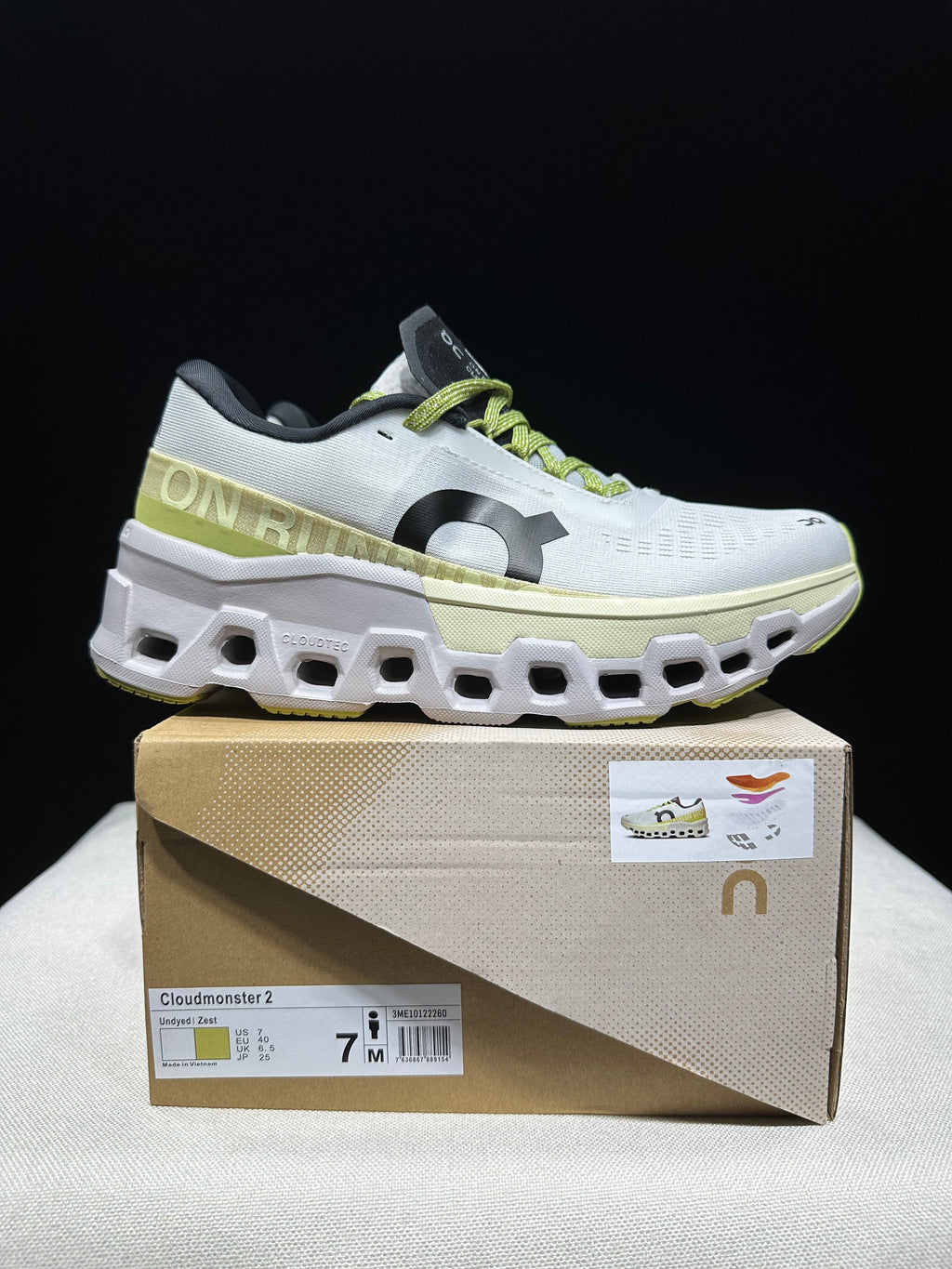 Side view of a white and lime Cloudmonster 2 shoe on its box.