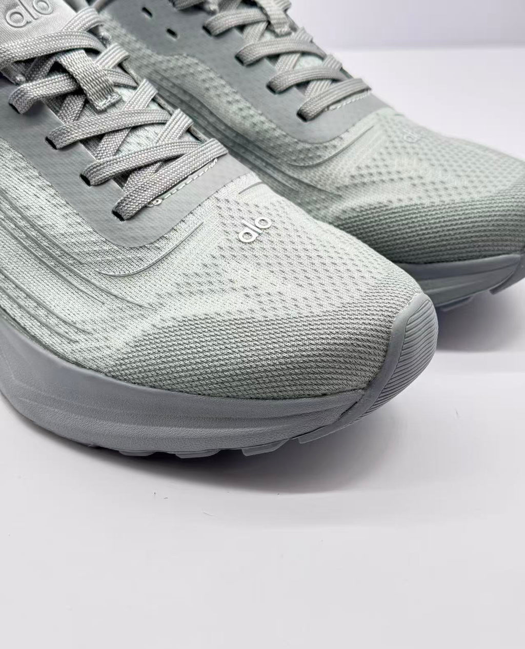 Close-up of the gray textured toe box, flat laces, tongue, and Alo logo.