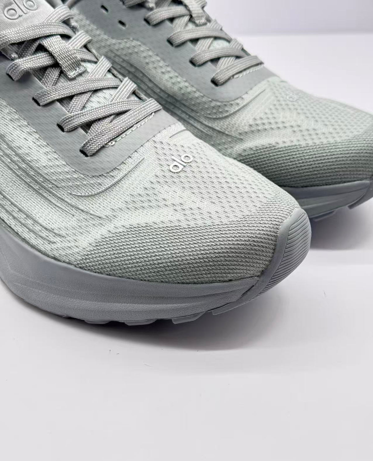 Close-up of the gray textured toe box, flat laces, tongue, and Alo logo.