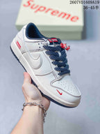 White Nike Dunk Low sneaker with navy patterned laces, red accent details and a decorative hanging accessory.