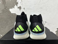 Rear view of black basketball shoes with white midsoles and neon-green Adidas heel logos.