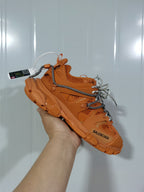 Orange Balenciaga Track 7000 sneaker held at an angle, showing the layered sole, mesh panels, overlays, and contrasting laces.