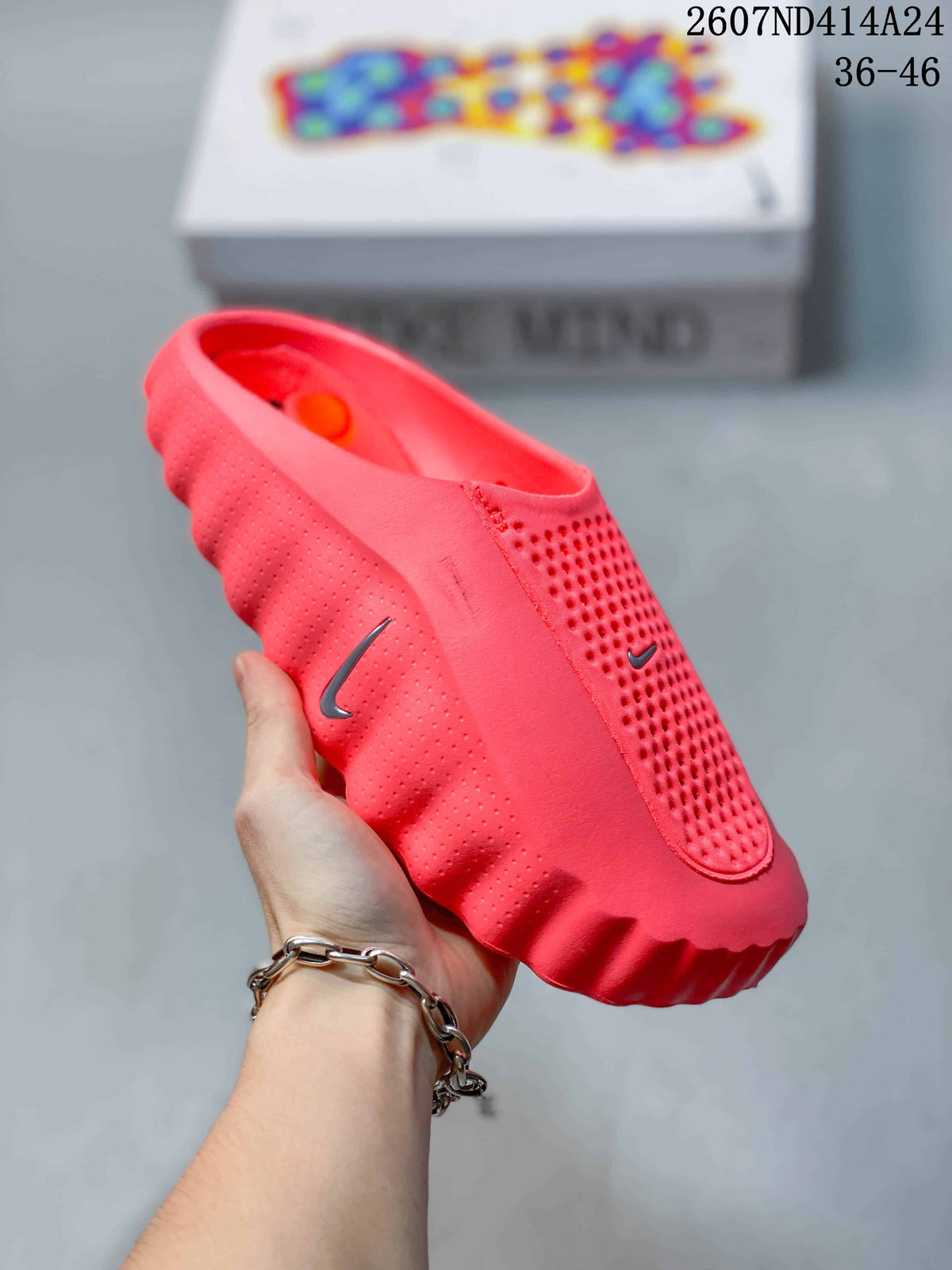 Angled side view of the coral-red Nike Mind 001 mule showing the open heel, perforated side panel, Nike Swoosh, and ridged outsole.
