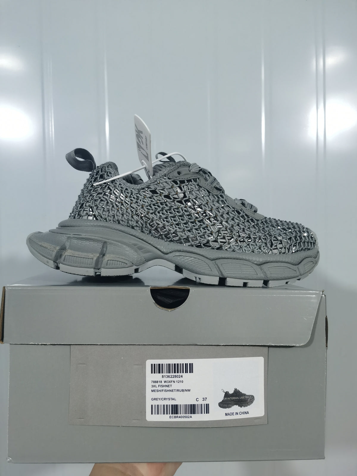 Side profile of the sneaker resting on its box; the box label shows model 1210, color Grey/Crystal, and size C 37.