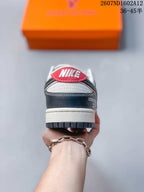 Rear view of a low-top sneaker showing a red heel tab, dark heel overlay, white midsole and dark outsole.