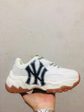 White chunky sneaker with a large navy MLB side logo, white laces, layered sole, and gum-colored outsole.