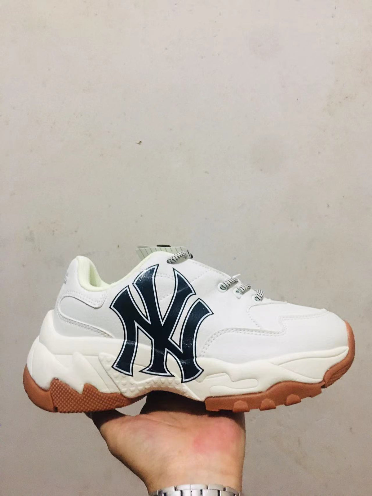 White chunky sneaker with a large navy MLB side logo, white laces, layered sole, and gum-colored outsole.