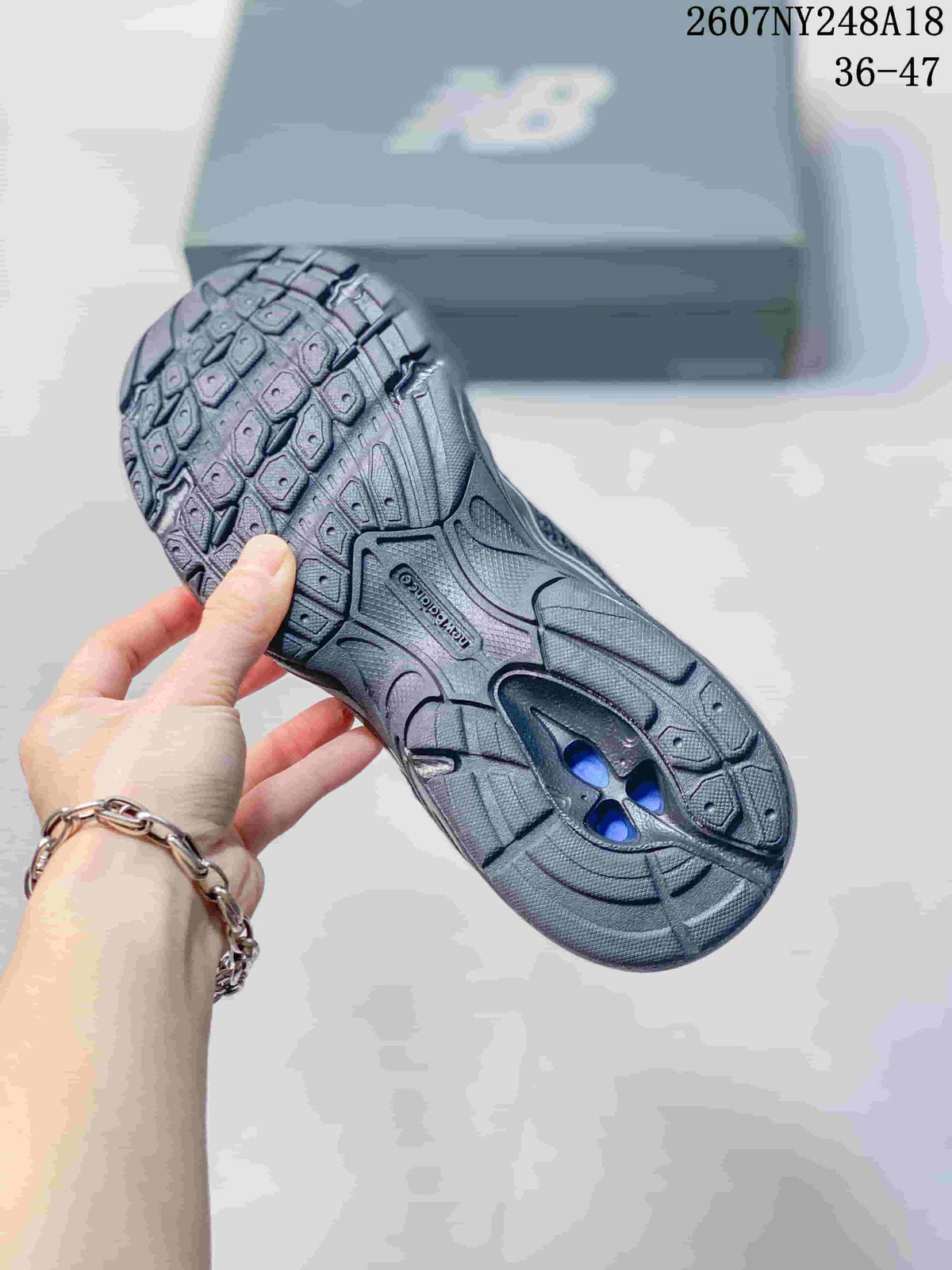 Underside view of a black and gray sneaker showing the patterned rubber outsole and central traction section.