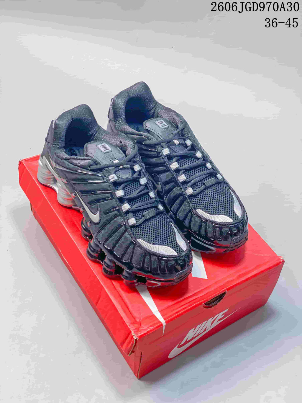 Pair of dark Nike Shox TL sneakers with silver accents on a red shoebox