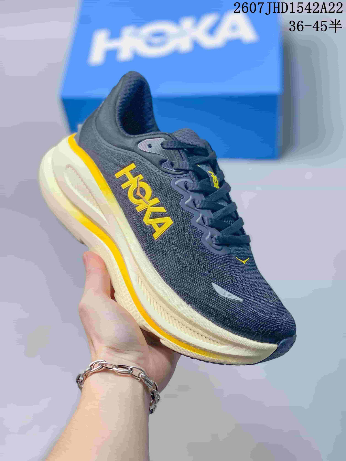 Angled side view of the charcoal-black HOKA sneaker with yellow branding and a cream-colored sole.