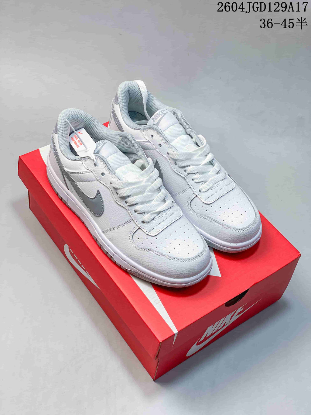 Pair of white low-top sneakers with gray Swoosh details on a red shoe box