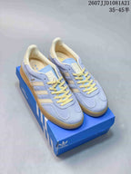 Pair of light blue and cream adidas Originals Gazelle Indoor sneakers displayed on a blue shoebox.
