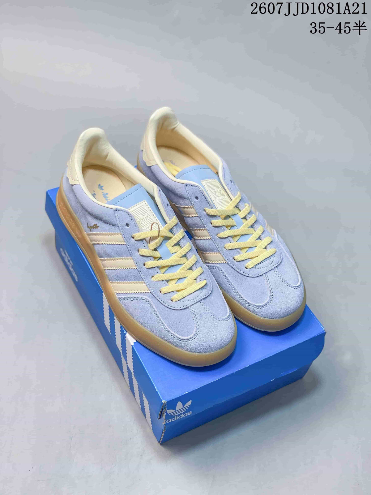 Pair of light blue and cream adidas Originals Gazelle Indoor sneakers displayed on a blue shoebox.