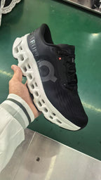 Handheld view of a black On running sneaker showing the side logo, lace area, and white midsole.