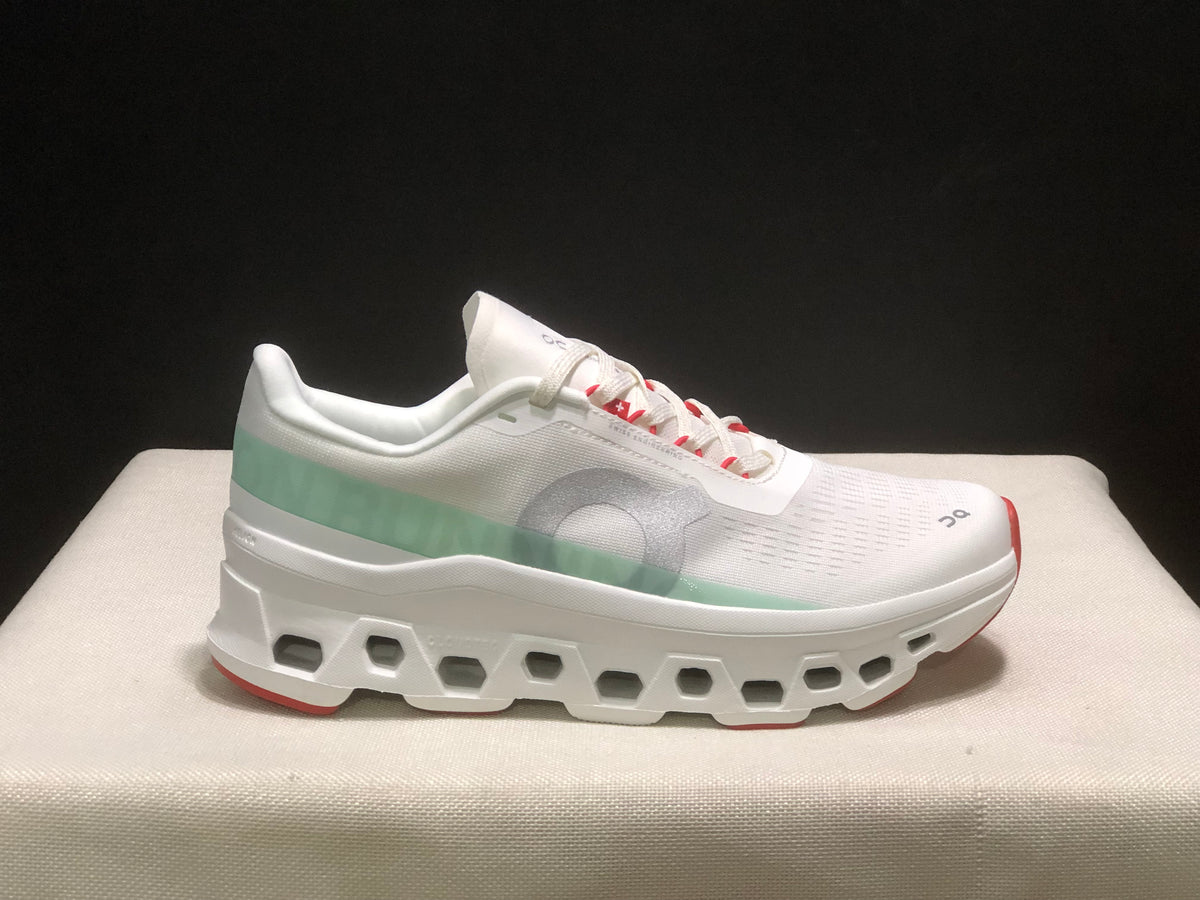 Side profile of one white On Cloudmonster 1 sneaker showing the lace-up upper, pale green heel panel, gray side logo, and red outsole edge.