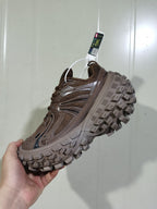 Side view of a coffee-brown chunky sneaker showing the mesh upper, layered side panels, and thick lugged outsole.