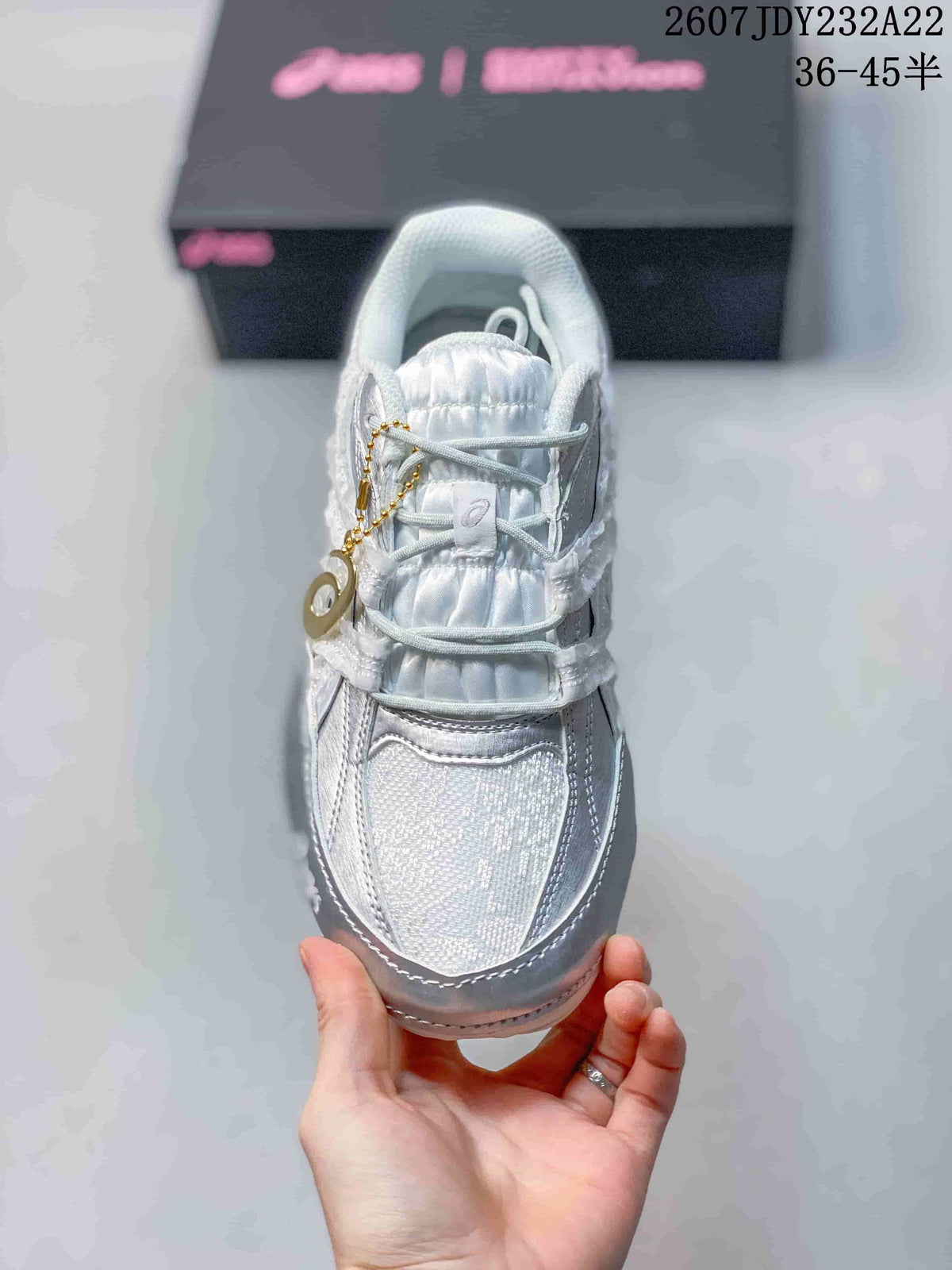 Top view of the sneaker showing the padded tongue, layered lace area, mesh-like toe panel, and gold-tone lace charm.