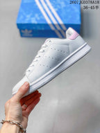 Side view showing the white upper, perforated panel, pink heel accent, laces, and flat rubber sole.