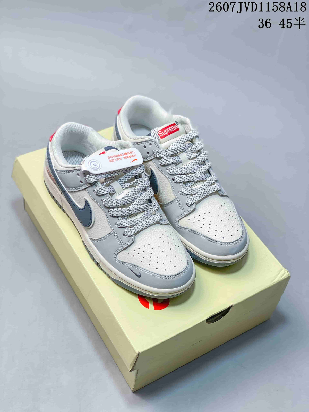 Pair of light gray, white, and dark gray Nike SB Dunk Low sneakers displayed on a branded shoe box.