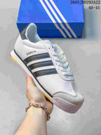 White Adidas Samoa sneaker with dark side stripes, gray toe detailing and multicolor sole accents.