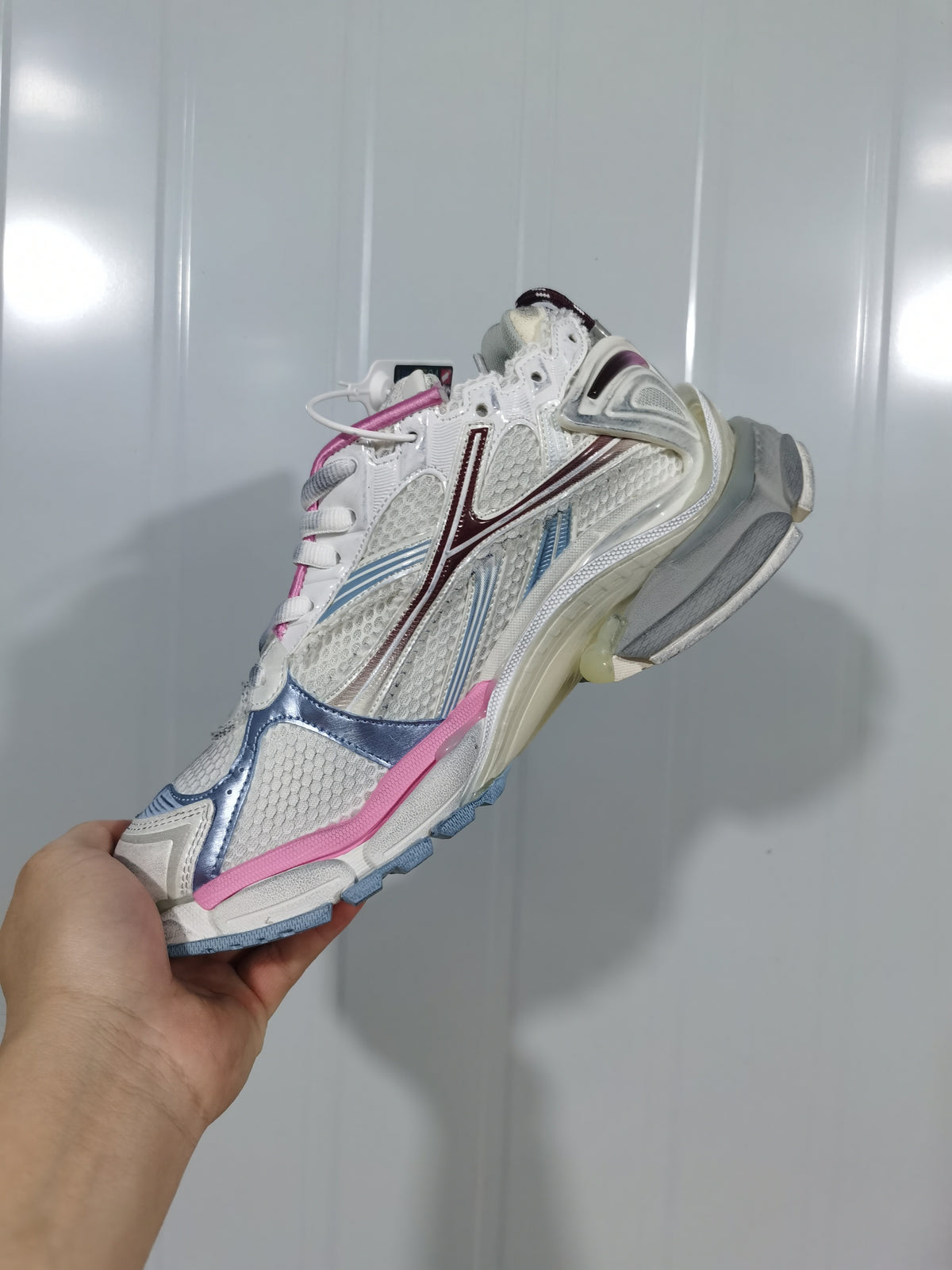 Side view of the white Balenciaga Runner 3120 sneaker showing layered panels, mesh-look sections, blue and pink accents, and a chunky sole.