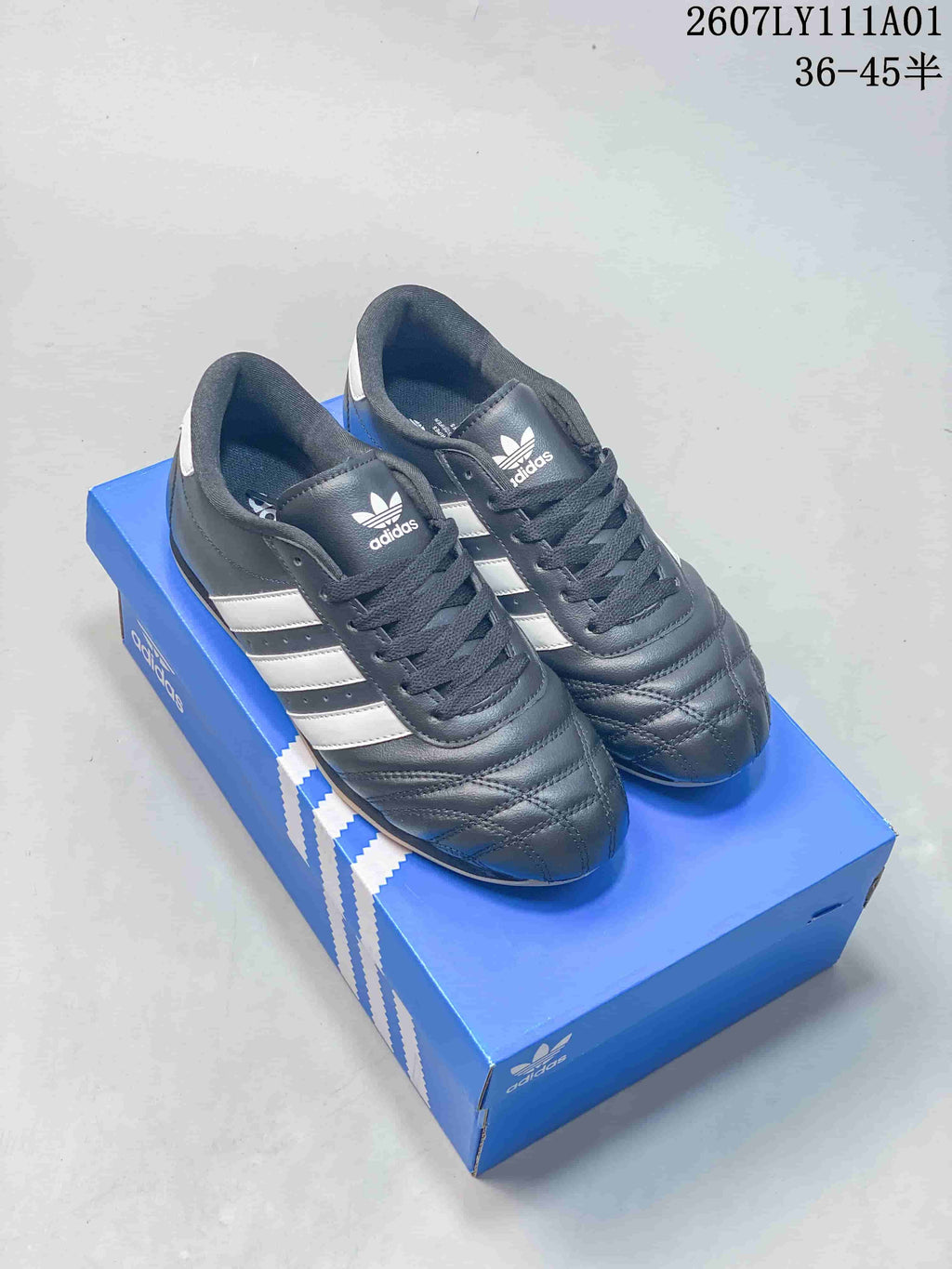 Dark gray Adidas Originals Taekwondo low-top sneakers with white stripes on a blue box
