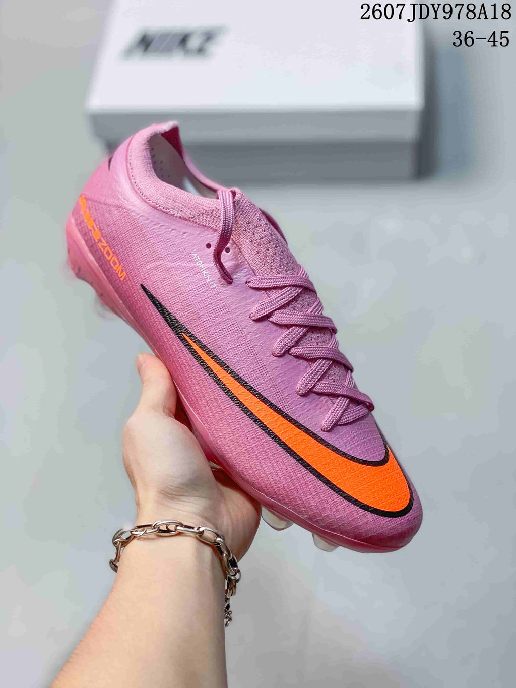 Pink Nike soccer cleat with orange and black side graphics and molded studs.