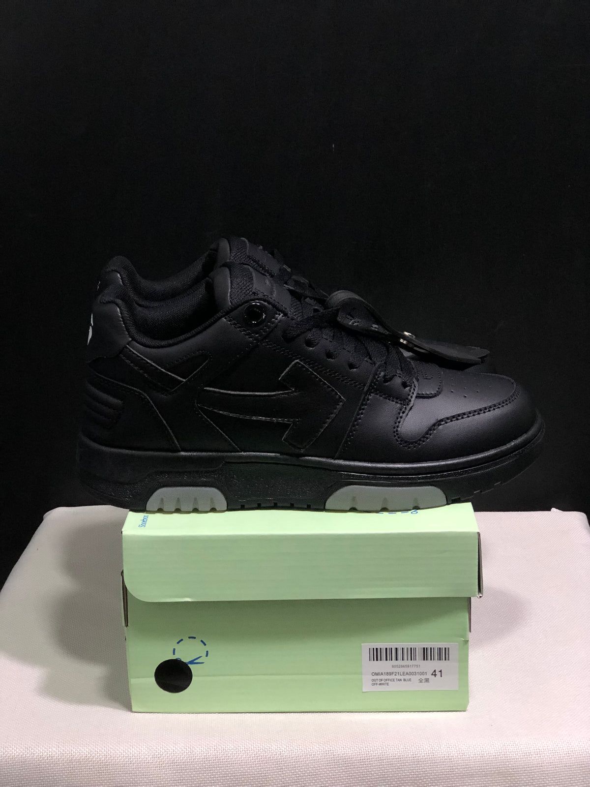 Side view of a black low-top sneaker with layered panel detailing, tonal laces and light outsole sections; size 41 is visible on the box label.