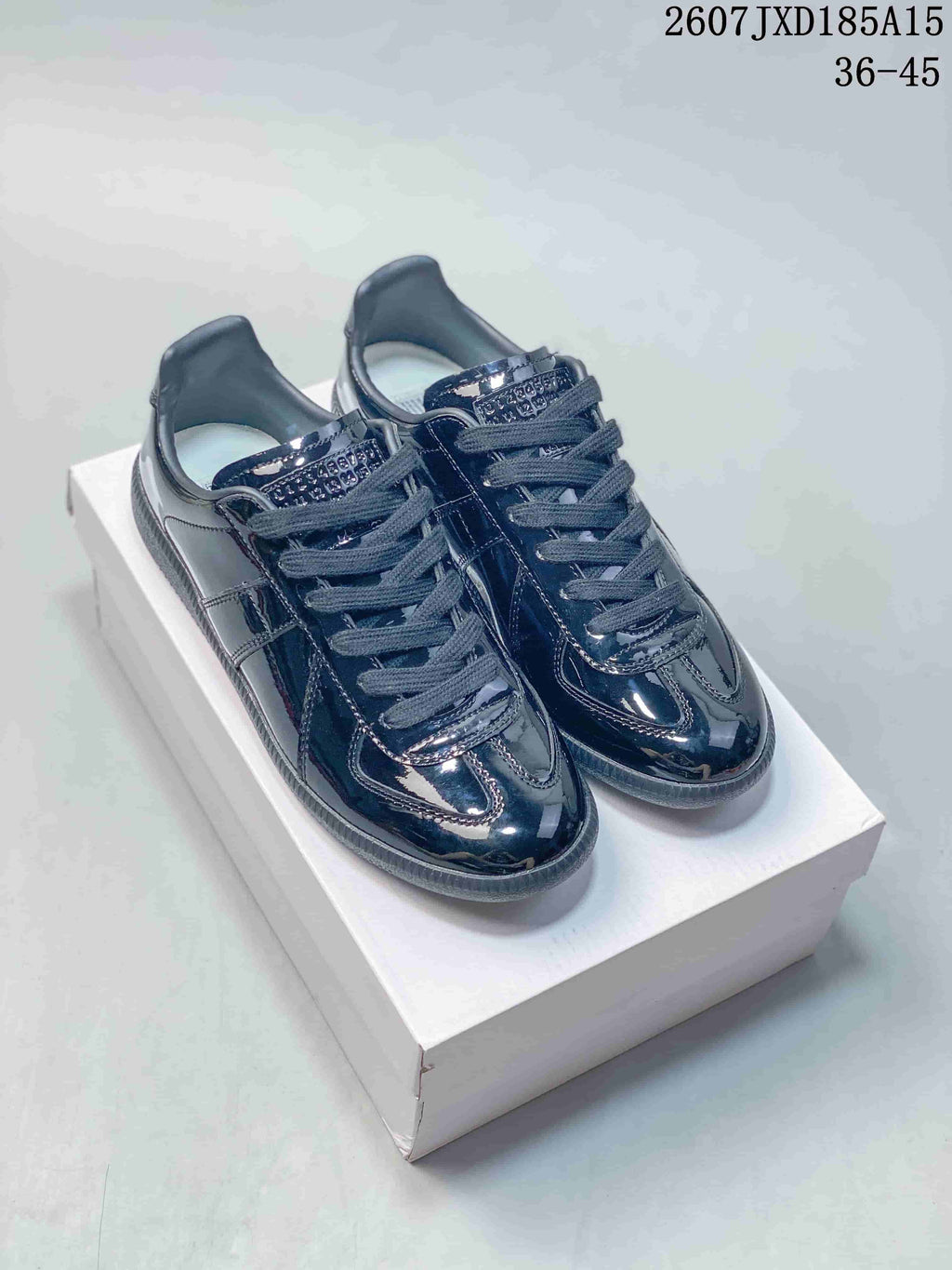 Pair of dark glossy Maison Margiela low-top sneakers displayed on a white shoebox.
