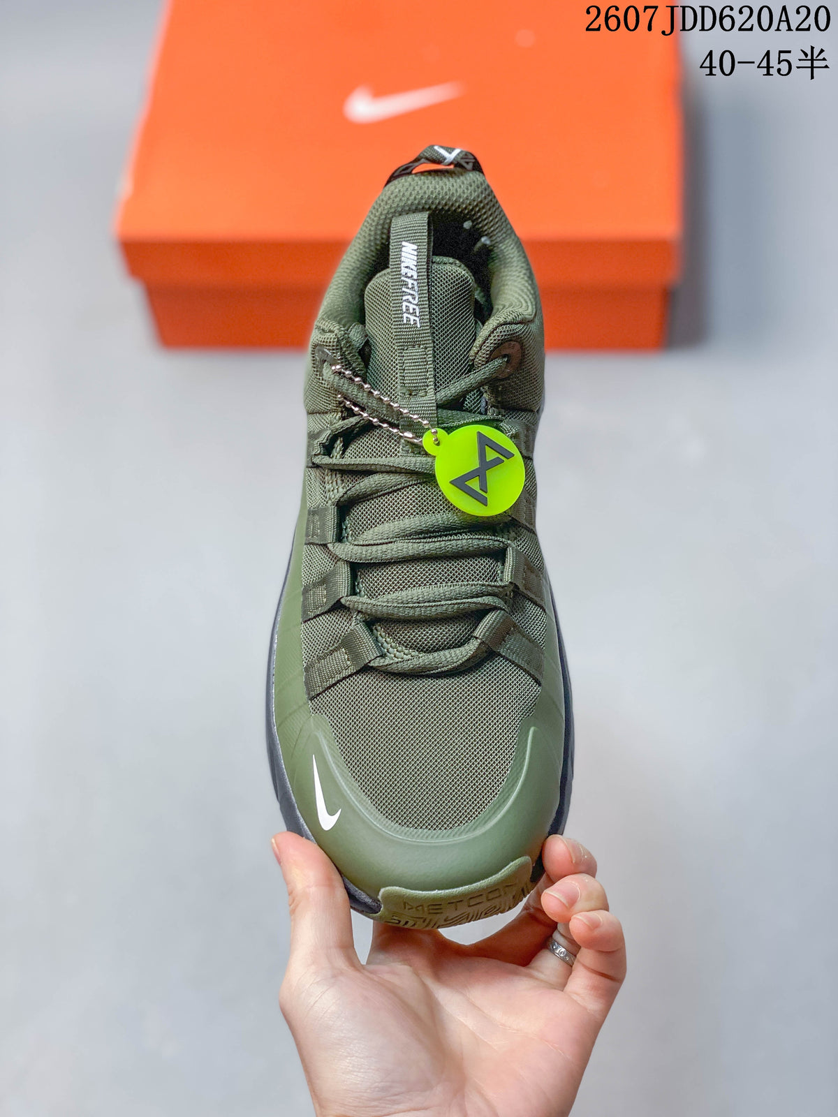 Top view of the olive green Nike training shoe showing the mesh toe box, layered lacing system, tongue branding and neon green accessory tag.